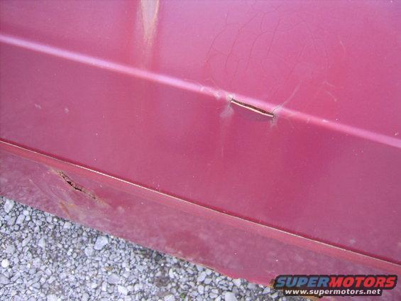 Red car door with rust near the bottom and a crack on the body line