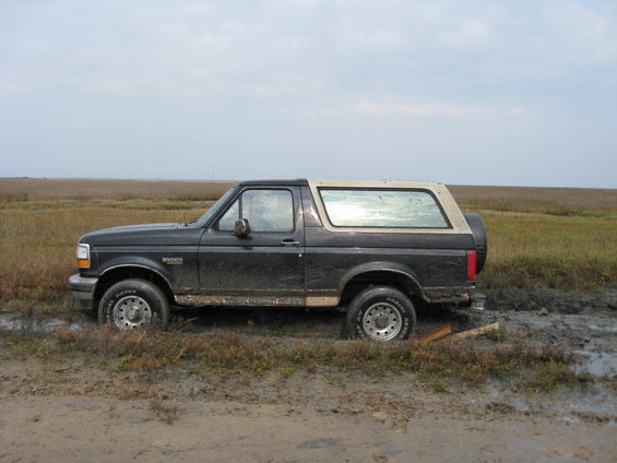 Black Ford Bronco stuck in mud, side view, tan removable top, spare tire on rear