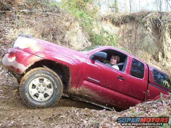 Red Toyota Tacoma pickup truck with a person inside, stuck in a muddy ditch off-road