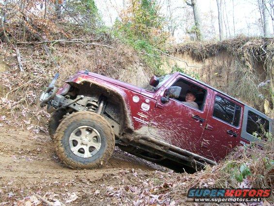 Red Jeep Wrangler climbing a muddy hill with a person inside
