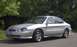 1998 Ford Taurus - A silver 1998 Ford Taurus is parked on a street with trees and foliage visible behind it.