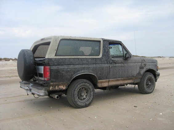 Mud-covered black 1994 Ford Bronco with spare tire on rear, seen from the 3/4 front