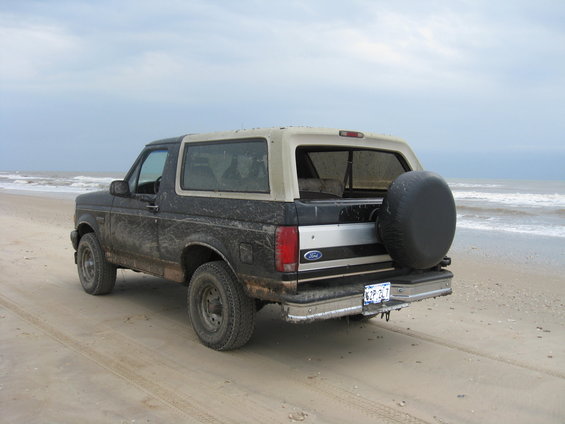 1994 Ford Bronco parked on a sandy beach with the ocean in the background