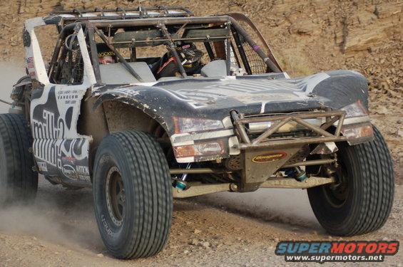 Off-road race truck with roll cage and large tires driving on a dirt track