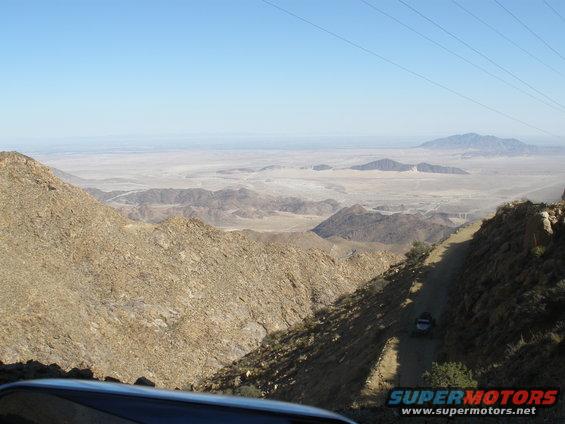 Desert landscape with mountains, a dirt road, and a single vehicle in the distance