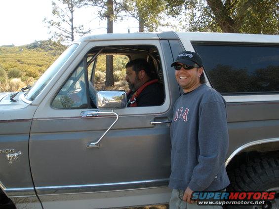 Gray Ford Bronco with a white roof, two men standing outside and inside, off-road tires visible