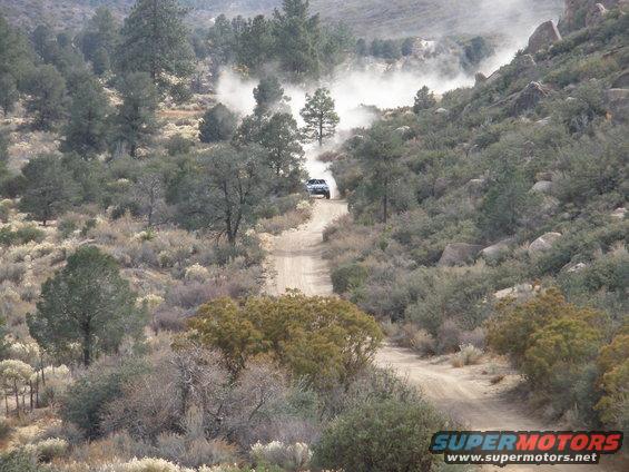 SUV kicking up dust on a winding dirt road through arid hills and trees