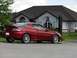 1993 Mazda MX-3 - A red coupe is parked on a paved surface in front of a modern house with a dark roof.