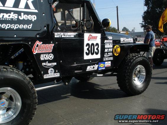 Black off-road Jeep with number 303, Currie, BFGoodrich, and other sponsor decals. Another vehicle is visible to the right