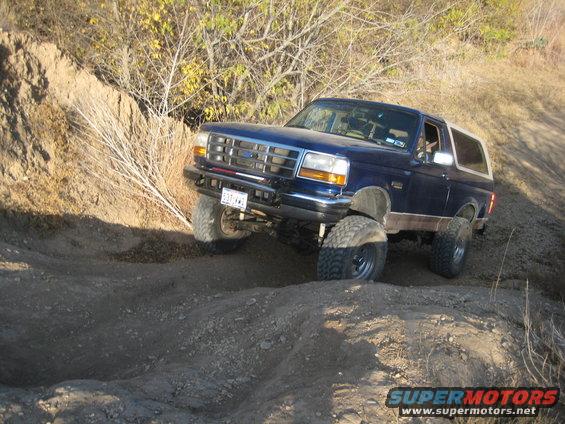 Blue Ford Bronco with lifted suspension and off-road tires navigating a dirt trail