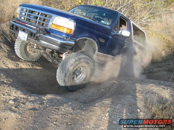 Blue 1996 Ford Bronco driving off-road, kicking up dust