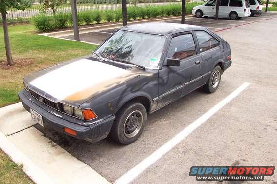 Dark gray hatchback parked in a lot, hood is faded. License plate visible