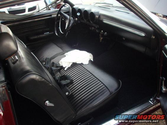 Interior of a classic car, showing black vinyl seats, dashboard with three gauges, and steering wheel