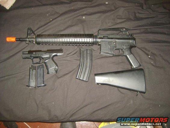 AR-15 style rifle, pistol, and extra magazines laid out on a black cloth