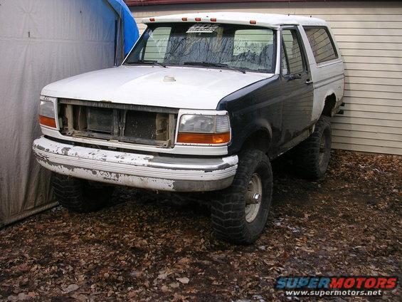 White and black Ford Bronco with missing grille, lifted suspension, and off-road tires