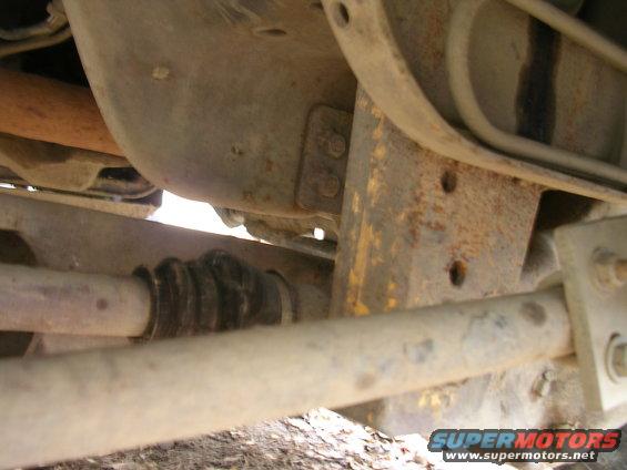 Undercarriage view of a vehicle, showing a driveshaft with a rubber boot and rusty suspension components