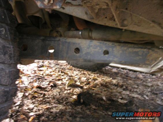 Undercarriage of a vehicle with a drive shaft and frame visible, covered in dirt and leaves
