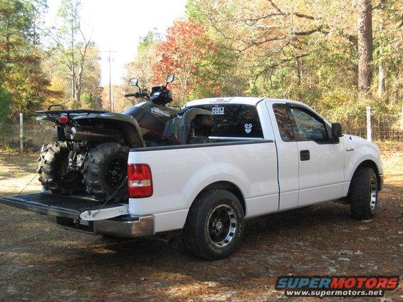 White pickup truck with an ATV in the bed, parked outdoors