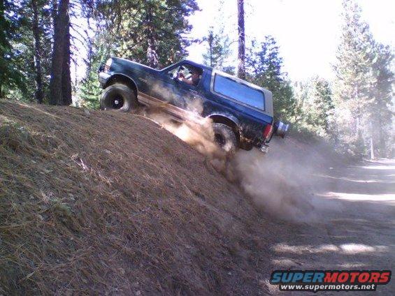 1995 Ford Bronco kicking up dust while driving down a dirt hill