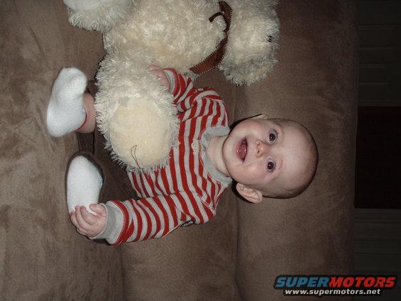 Baby in a striped shirt and white socks holding a teddy bear on a brown couch