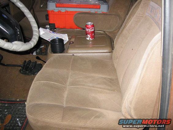 Vehicle interior with tan cloth seats, a Coca-Cola can on the center console, and a large orange toolbox behind the seats