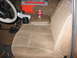 1987 Ford Bronco - The interior of this vehicle shows tan cloth seats and a center console with a drink and a toolbox.