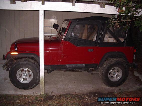 Red Jeep Wrangler with a black soft top, seen from the side under a white overhang