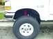 1995 Ford Bronco - Close-up of a lifted white truck's front wheel and fender, with visible red suspension components.
