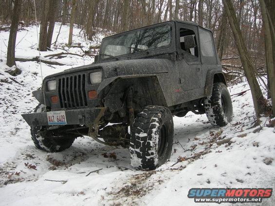 Dark gray 1991 Jeep Wrangler with a hardtop, off-road tires, and a custom bumper in a snowy wooded area