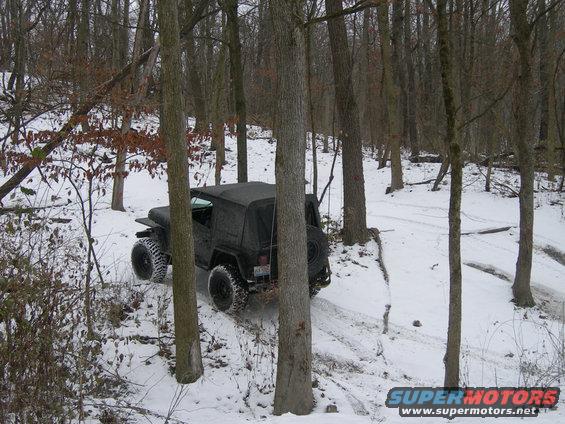 black Jeep Wrangler driving on snowy trail in woods