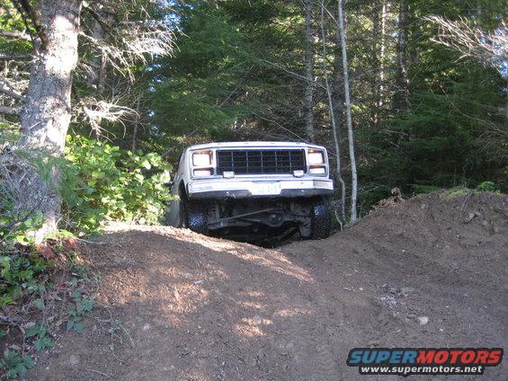 White SUV climbing a dirt mound in a wooded area. Supermotors.net logo visible