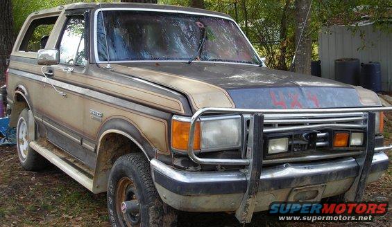Old Ford Bronco with a brush guard and two-tone paint. It has side steps and a 4x4 decal on the hood