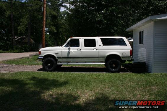 White 1991 Ford C-350 Centurion Conversions extended cab pickup truck with a camper shell, side view, parked on grass next to a white building
