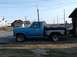 1983 Ford F-150 - A blue pickup truck is parked outdoors next to a building under a clear sky.