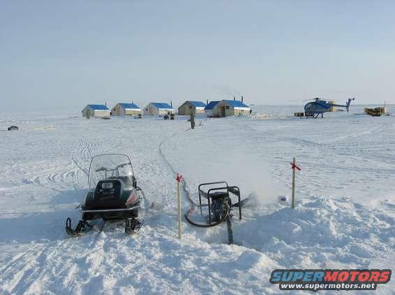 Snowmobile in foreground, helicopter and buildings in background on snowy plain