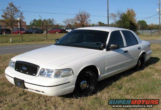 White Ford Crown Victoria parked on grass, front quarter view. Black grille and black steel wheels