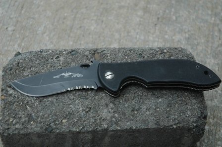 Black folding knife with serrated edge on a concrete block