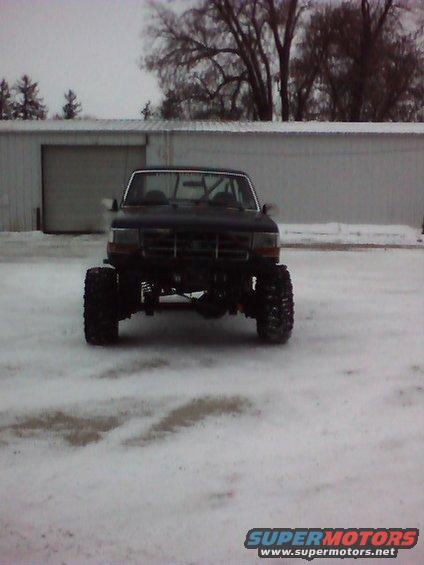 Front view of dark lifted Ford Bronco on big tires parked in snow near a metal building