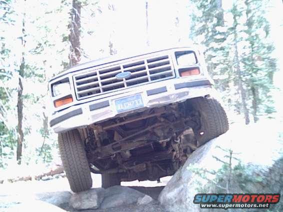 White Ford Bronco with a blue license plate, angled up on rocks, showing underside