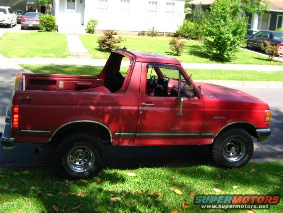 Red Ford Bronco parked on a grassy lawn, side view. The top is off