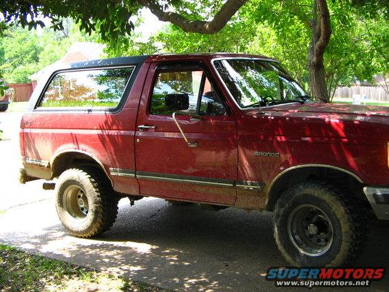 Red Ford Bronco with a black top, seen from the side at a 3/4 front angle