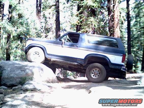 Two-tone blue and white Ford Bronco with off-road tires on rocks, side view