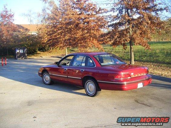1994 Ford Crown Victoria sedan, red, parked outside with trees in background