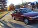 1994 Ford Crown Victoria - A maroon sedan is parked on a road during autumn, with a gas station visible in the distance.