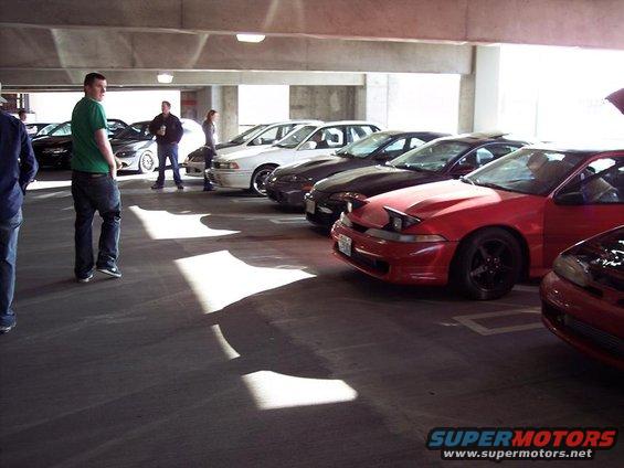Red 1991 Mitsubishi Eclipse with pop-up headlights parked in a garage, other cars visible