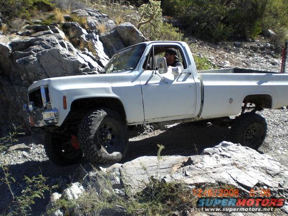 White pickup truck with large tires driving over rocks on a trail