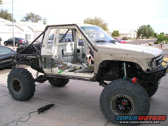 Modified pickup truck with large tires and roll cage, doors removed, in a driveway