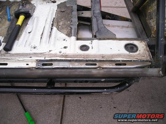 Modified truck frame with roll cage and running boards, showing rust and repair work