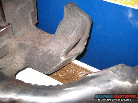 Close-up of a cast iron engine exhaust manifold with a curved pipe section