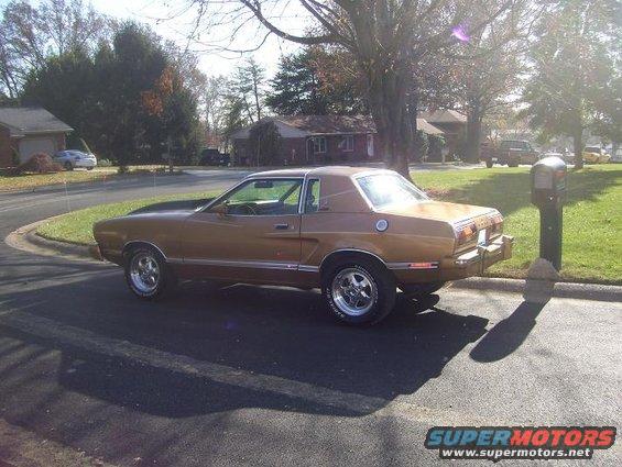 Brown 1977 Ford Mustang II coupe parked on asphalt, side view, chrome wheels, some sun flare